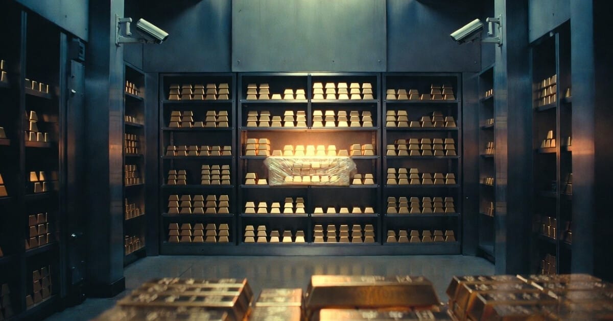 Central bank gold vault with rows of gold bars stacked on steel shelves. A new shipment of wrapped gold bars sits illuminated on a middle shelf. Security cameras visible in upper corners.
