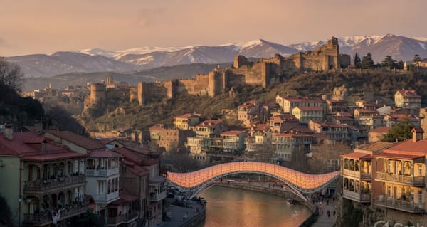 Golden-hour view of Tbilisi old town with the Narikala fortress, the Mtkvari River and the Bridge of Peace, Georgia.